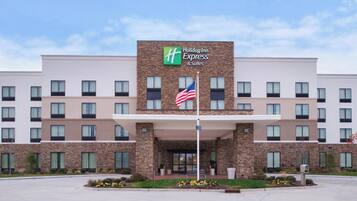 Un hôtel Holiday Inn Express & Suites doté d’une façade en pierre, de nombreuses fenêtres et arborant le drapeau américain.