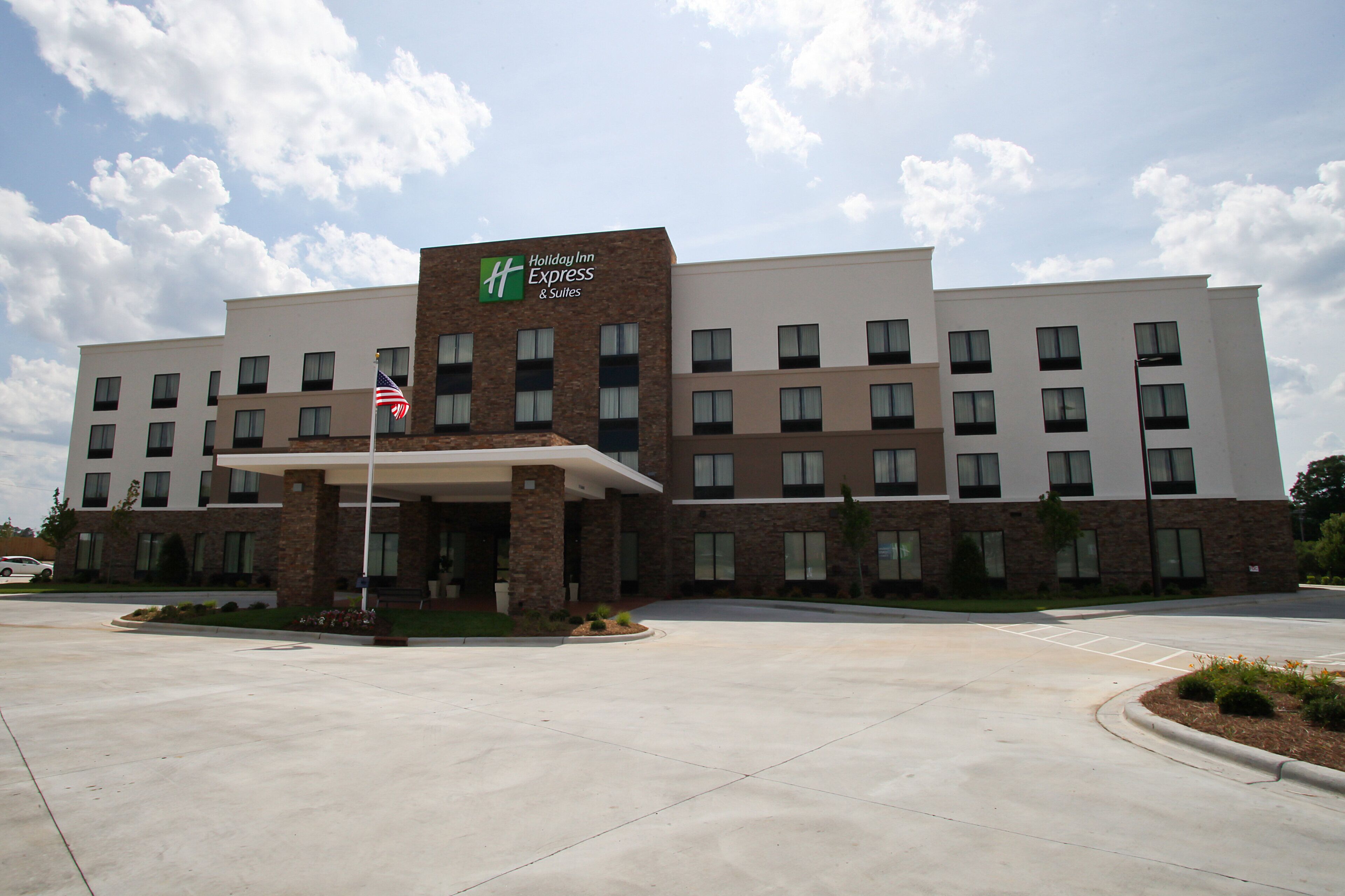 A Holiday Inn Express & Suites hotel with a brick facade, multiple windows, and a flagpole with an American flag.