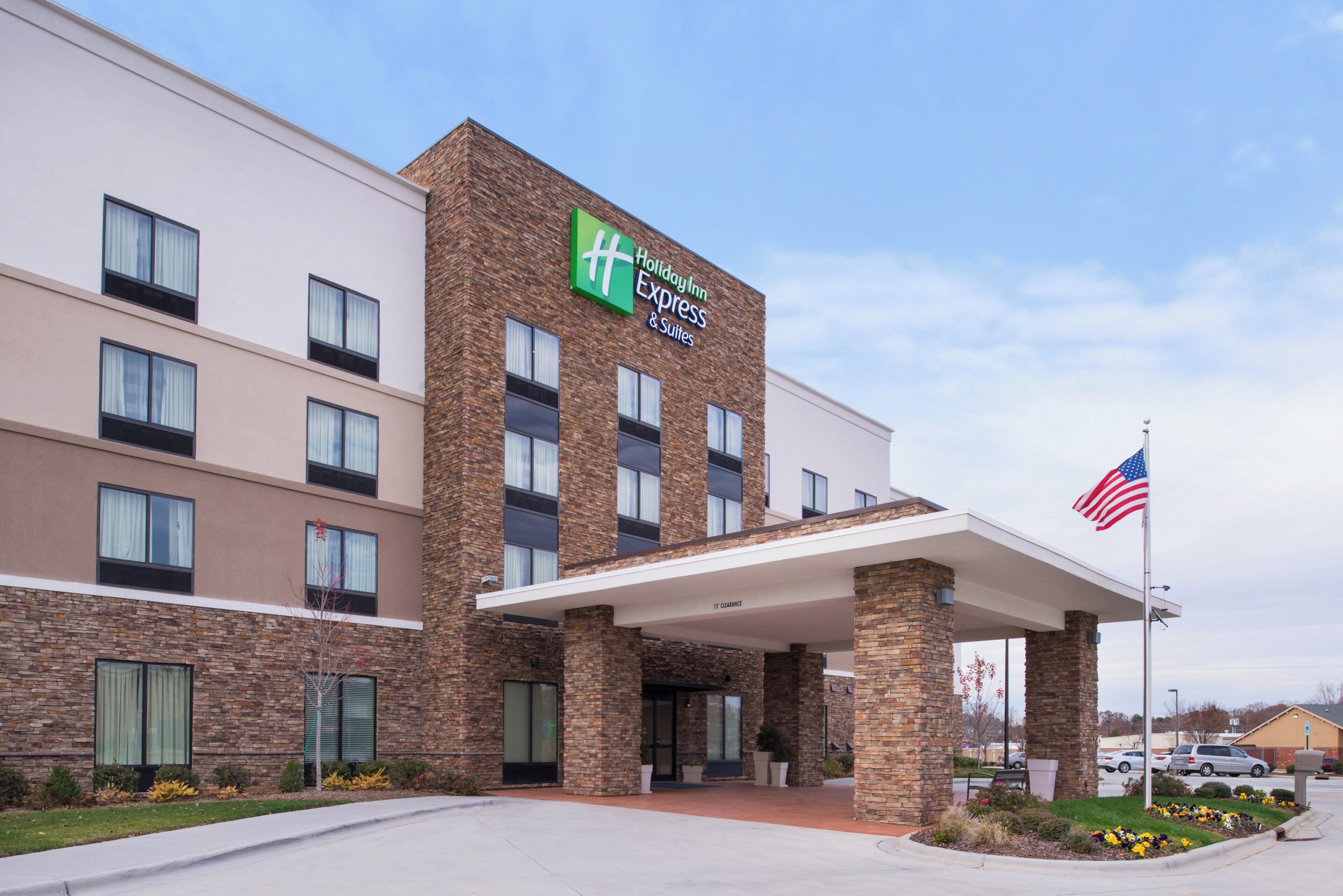 Un hotel Holiday Inn Express & Suites con fachada de ladrillo, múltiples ventanas y una bandera estadounidense.