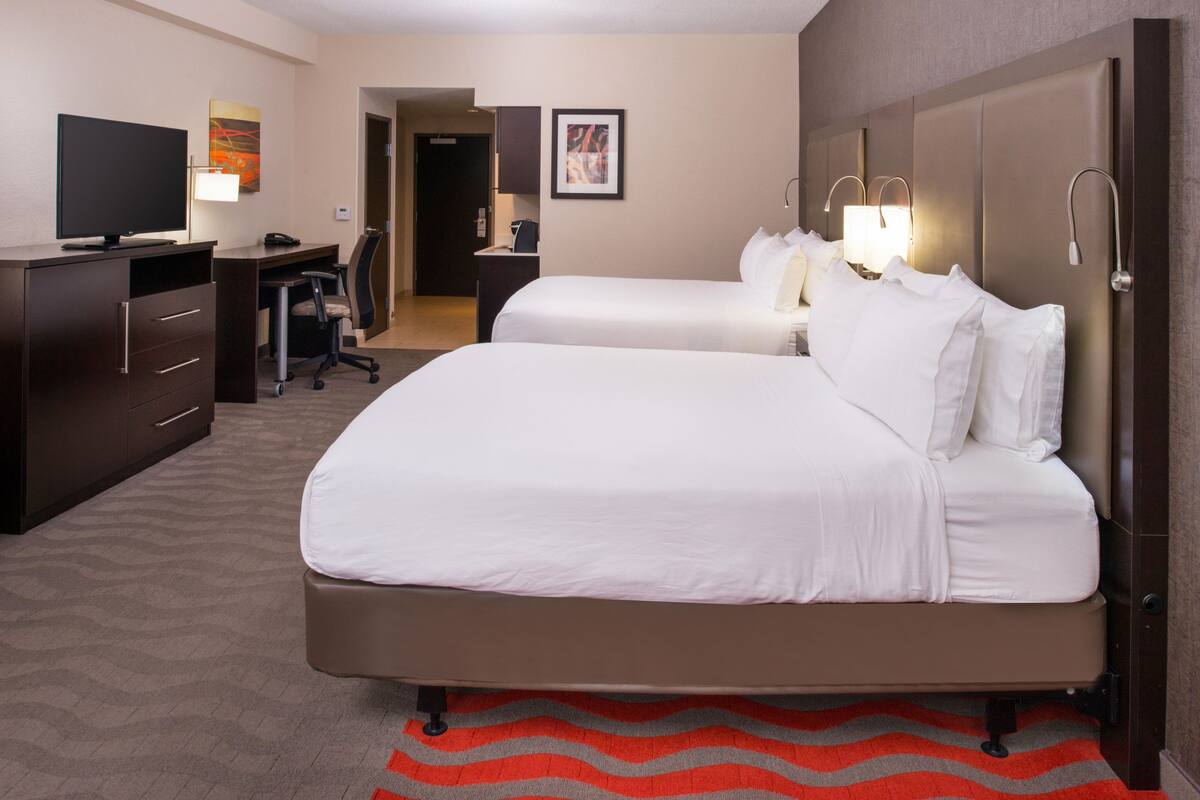 A hotel room with two beds, a desk, a chair, a television, and a lamp.