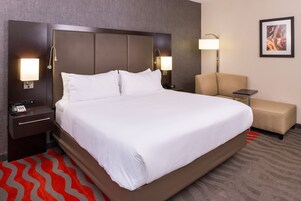 Una habitación de hotel con una cama grande, dos mesitas de noche con lámparas, una silla y una pequeña mesa.