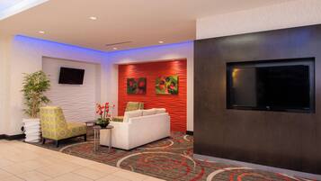 Eine moderne Lobby mit Flachbildfernseher, einer Couch, einem Sessel und einer Zimmerpflanze.