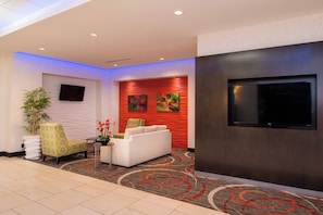 A modern lobby with a flat-screen TV, a sofa, a chair, and a potted plant. - Holiday Inn Express & Suites Monroe by IHG (Monroe)