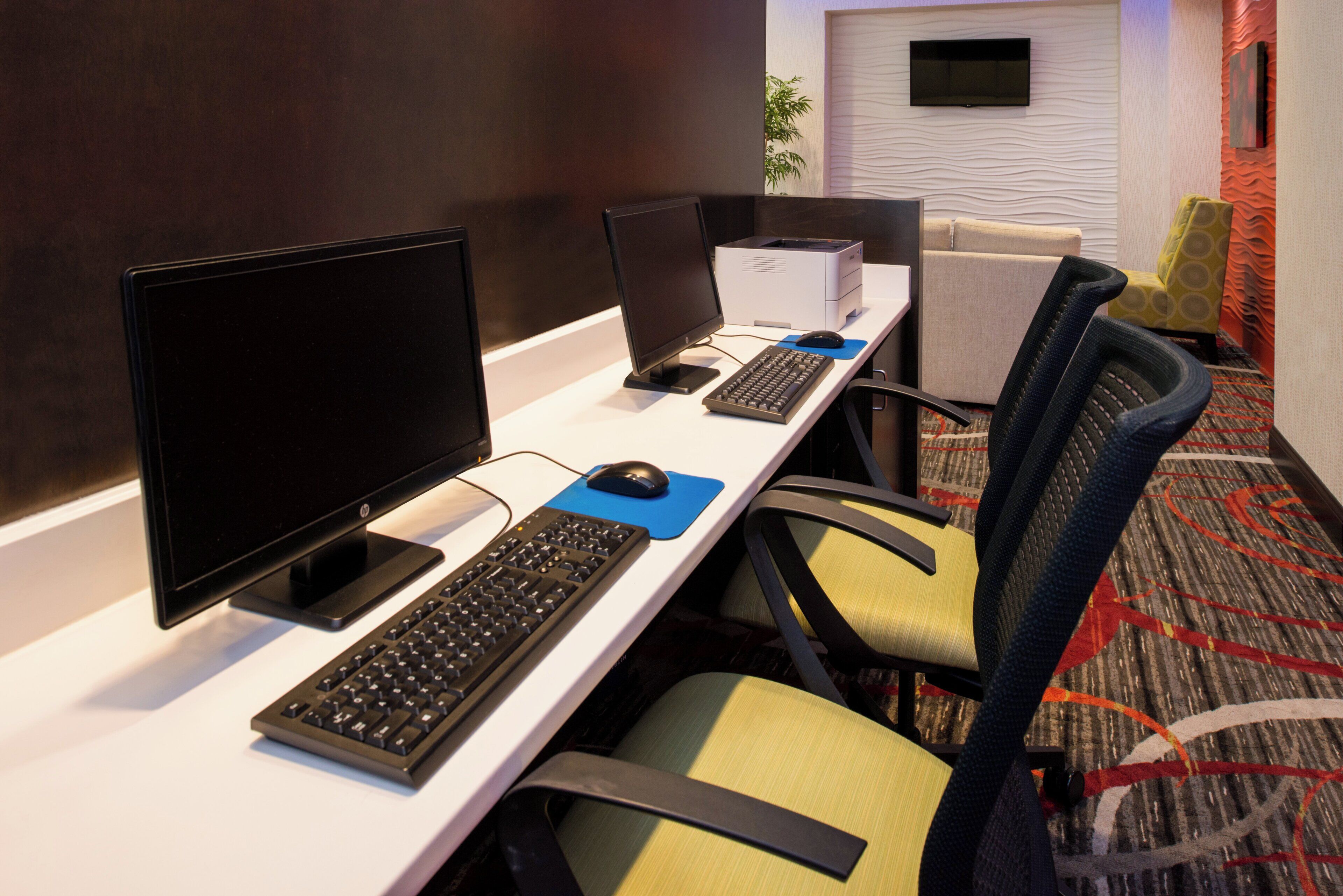 A hotel room with a desk equipped with a computer, keyboard, and mouse. There are chairs and a sofa in the room.