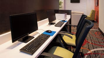 Een hotelkamer met een bureau, voorzien van een computer, toetsenbord en muis. Er staan stoelen en een bank in de kamer.