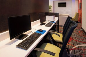 A hotel room with a desk equipped with a computer, keyboard, and mouse. There are chairs and a sofa in the room.