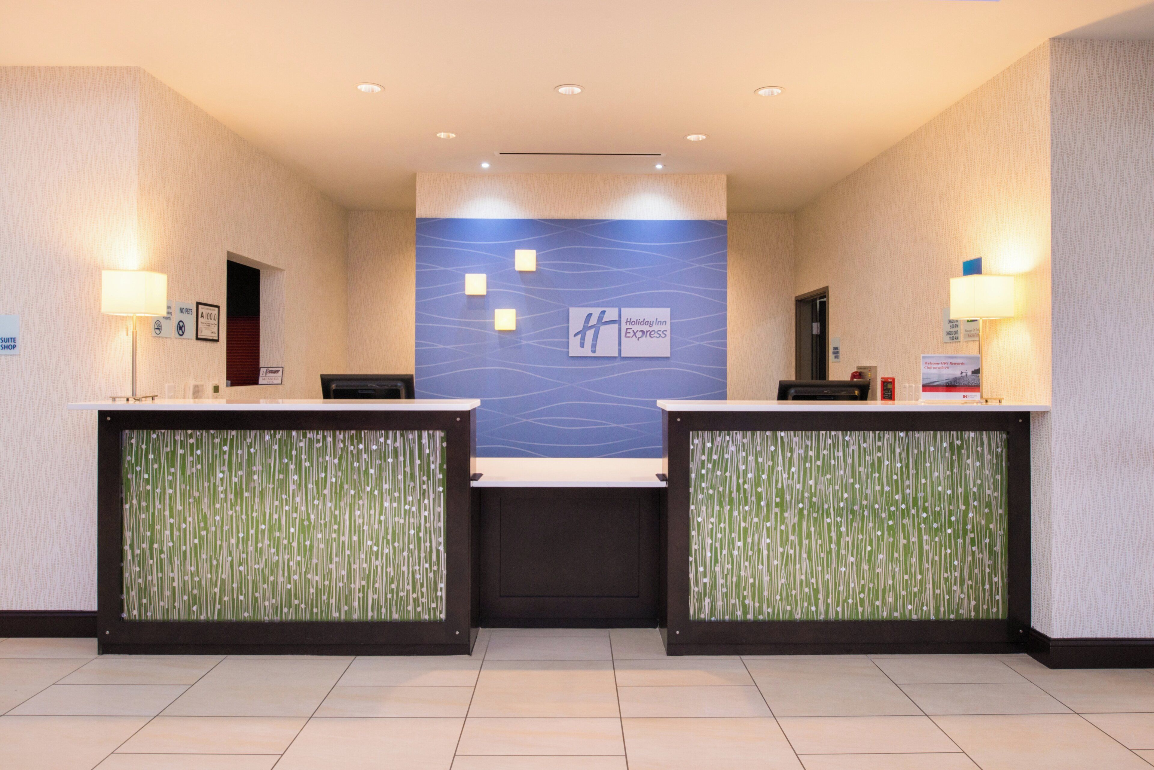 A reception area with two reception desks, a blue wall with the Holiday Inn Express logo, and a no pets sign.