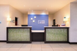 Zona de recepción con dos mostradores, una pared azul con el logotipo de Holiday Inn Express y un cartel que indica que no se permiten mascotas.