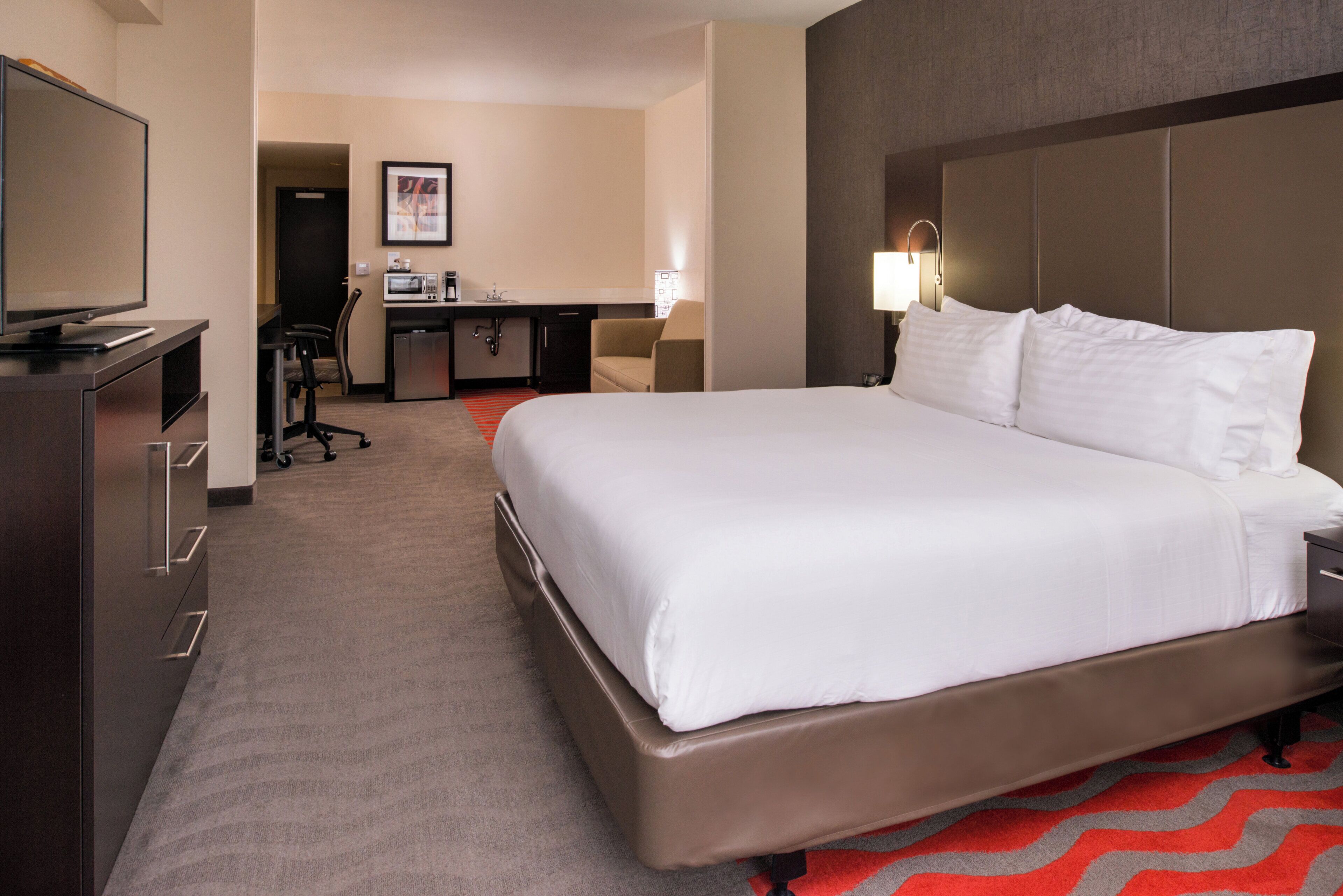Une chambre d’hôtel avec un grand lit, un bureau avec une chaise, une télévision et une petite kitchenette.