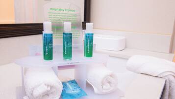 A bathroom counter with toiletries including lotion, shampoo, and conditioner, along with a sign about hospitality promise.