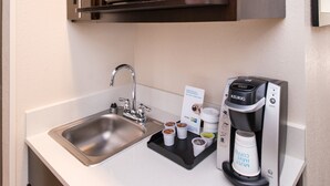 Eine Küchenzeile mit Spüle aus Edelstahl, einer Keurig-Kaffeemaschine und einer Ablage mit Kaffeekapseln und einer Tasse.