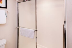 Un baño con mampara de vidrio, una toalla blanca colgada en la puerta y un inodoro blanco.