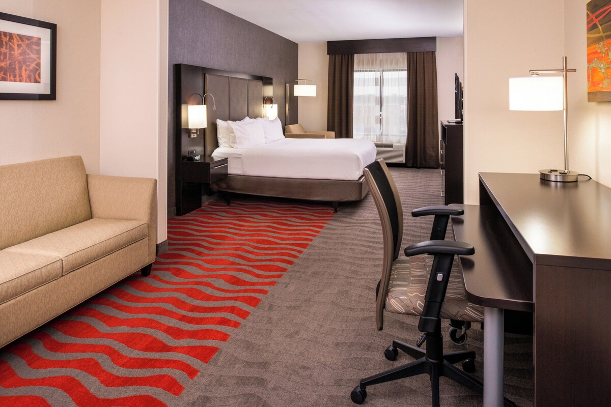 A hotel room with a bed, a desk, a chair, a sofa, and a red carpet.