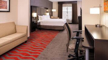 A hotel room with a bed, a desk, a chair, a sofa, and a red carpet.