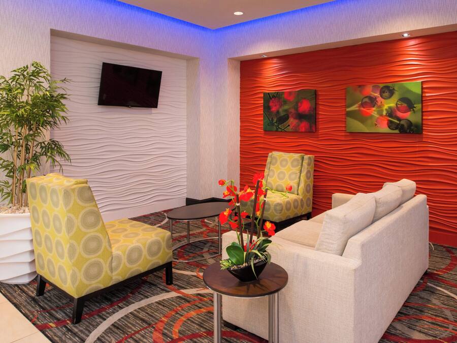 Eine Lobby mit einer Couch, Sesseln, einem kleinen Tisch, einer Topfpflanze und Kunstwerken an der Wand.