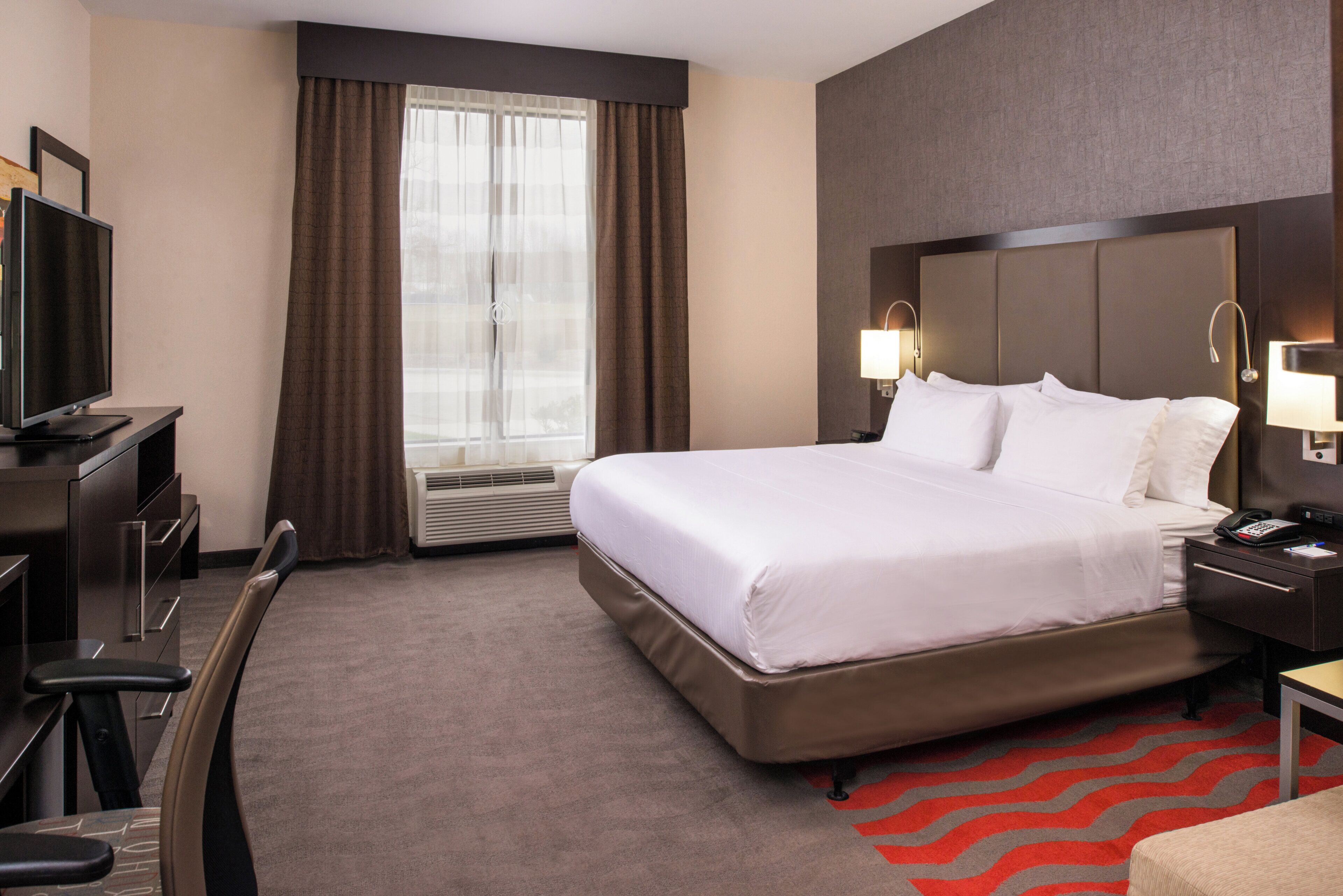 A hotel room with a bed, a desk, a chair, a television, and a window with curtains.