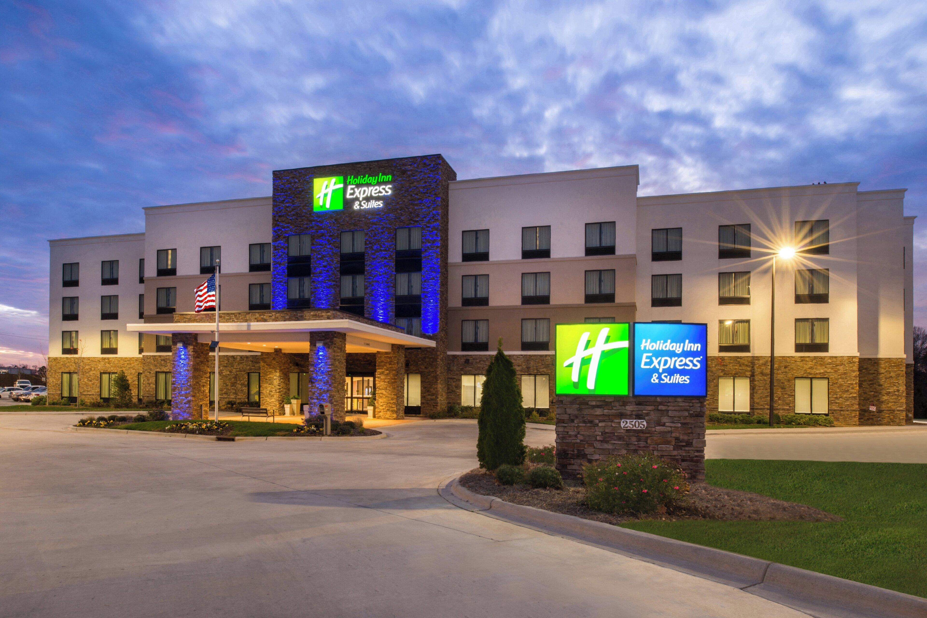 A Holiday Inn Express & Suites hotel with a stone facade, multiple windows, and an American flag.