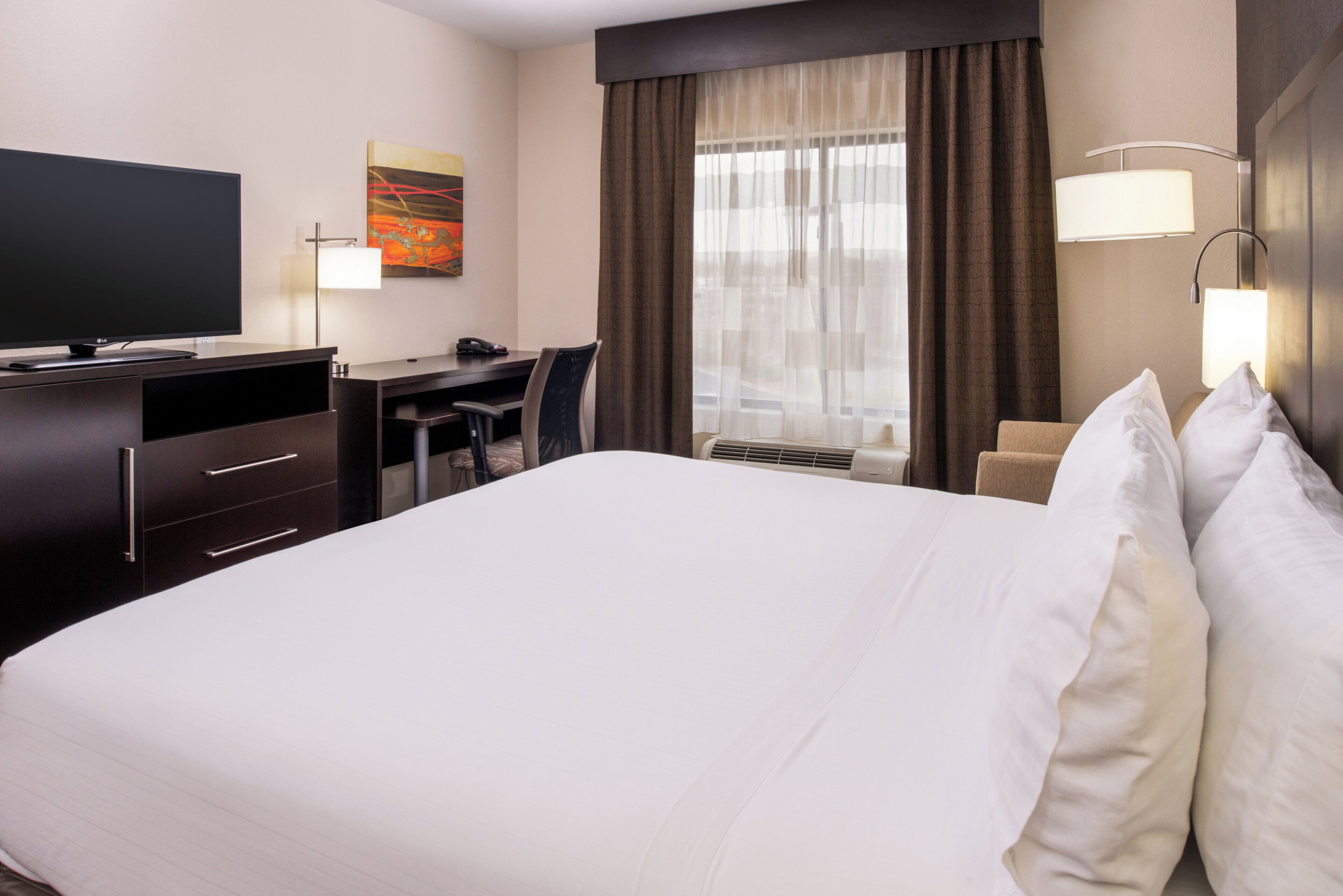 A hotel room with a bed, a desk, a chair, a television, and a window with curtains.