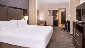 Ein Hotelzimmer mit einem großen Bett, einem Schreibtisch, einem Stuhl, einer Küchenzeile und einem Badezimmer.