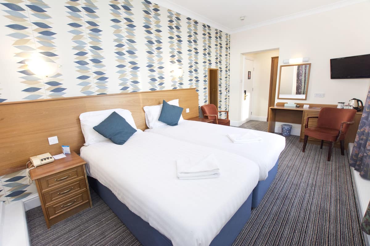 A hotel room with two beds, a desk, a chair, and a TV.