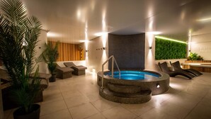 Un espace piscine intérieur moderne, doté d’un jacuzzi, de chaises longues et de plantes en pot.