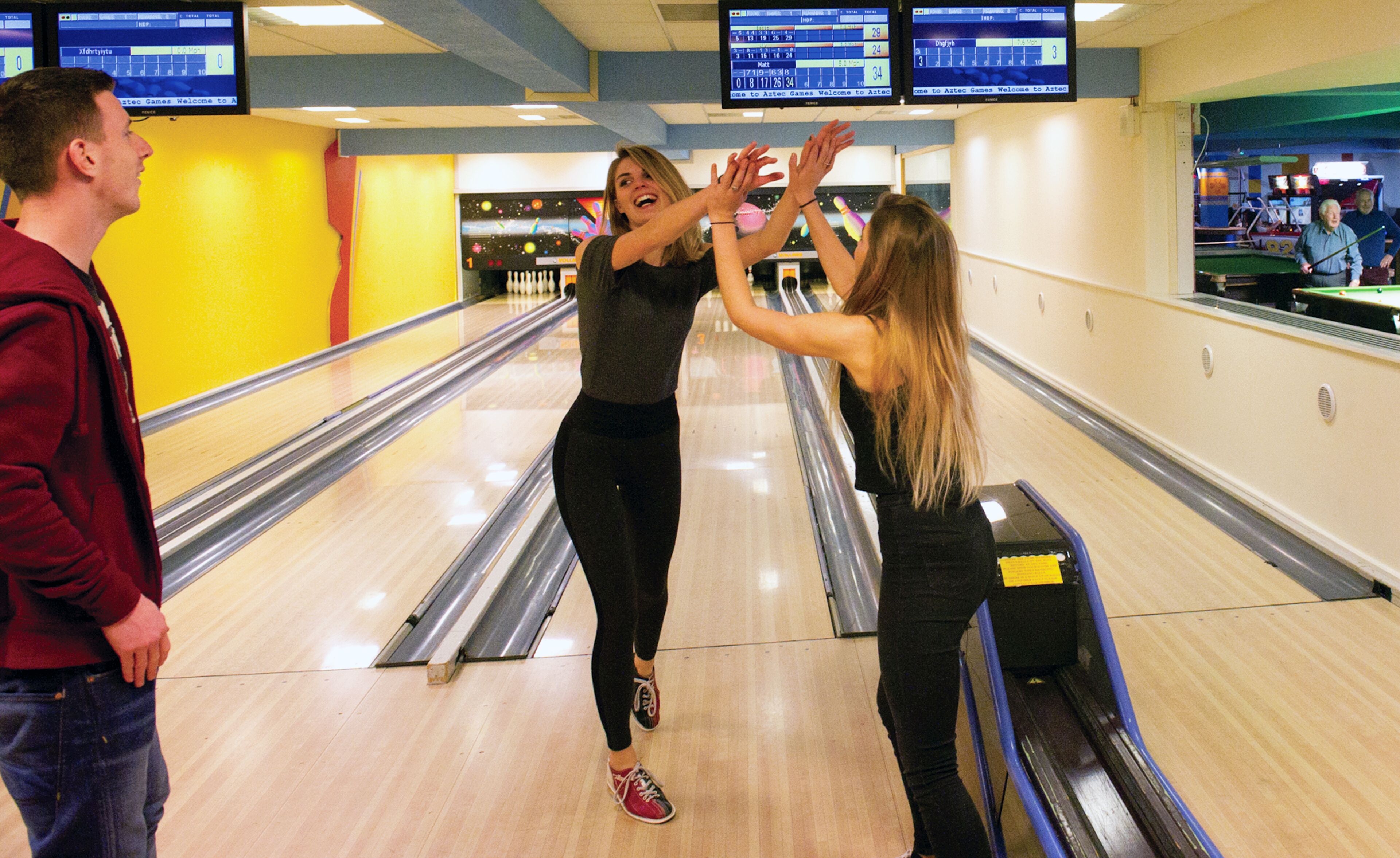 A bowling alley with lanes, a scoreboard, and a few people playing.