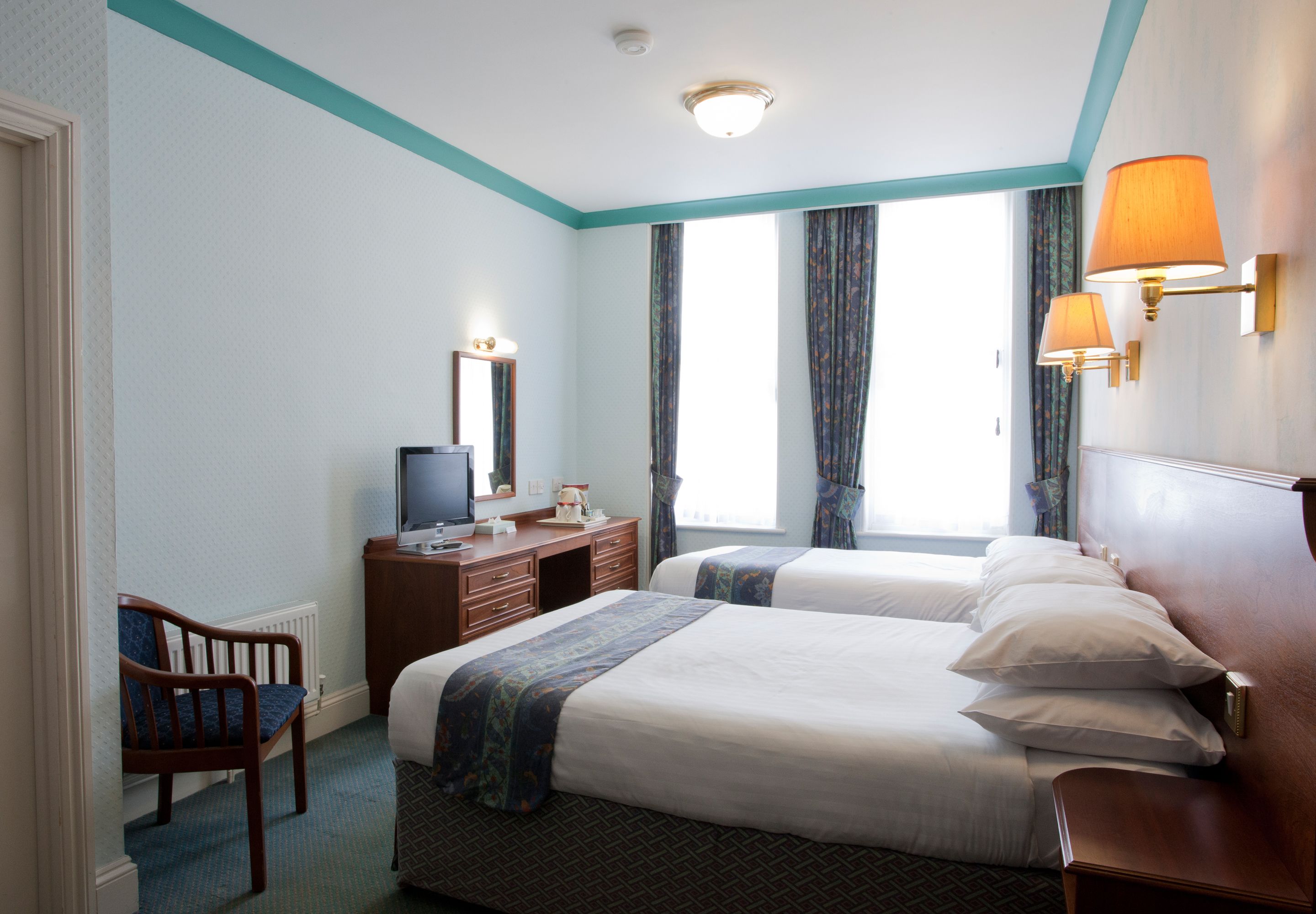 A hotel room with two beds, a desk with a television, a chair, and a window with curtains.