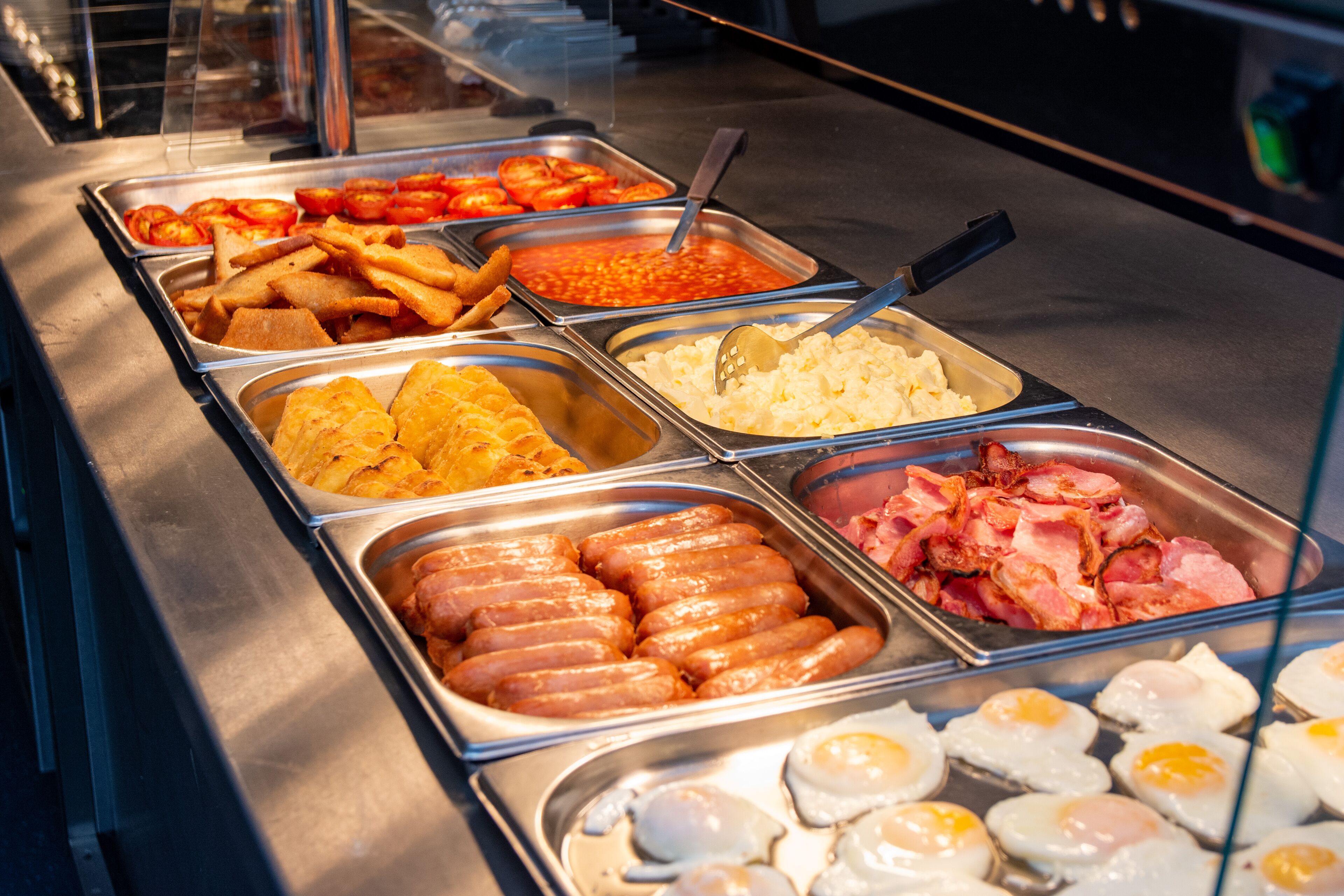 A buffet with various food options including sausages, eggs, and sauces.
