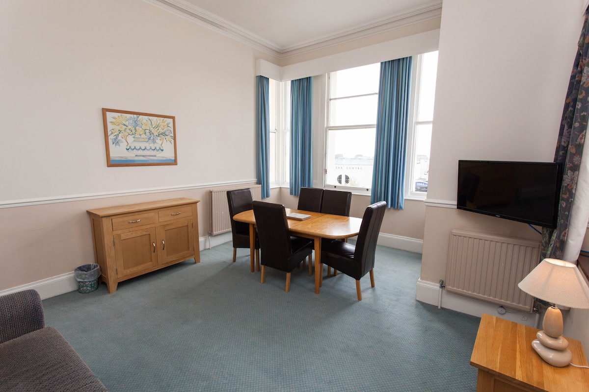 A room with a dining table, chairs, a television, a radiator, and a framed picture on the wall.