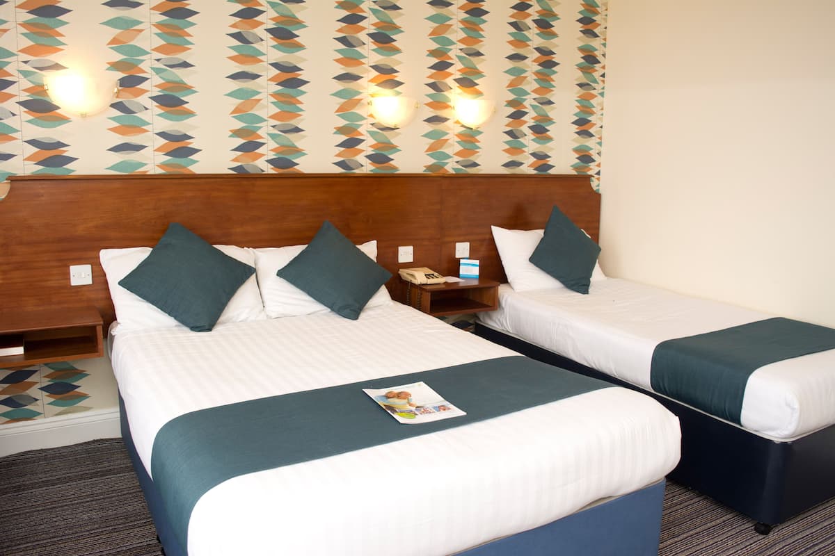 A hotel room with two beds, each with a wooden headboard, white bedding, and teal throw pillows. There is a nightstand with a phone and a magazine on the left bed.