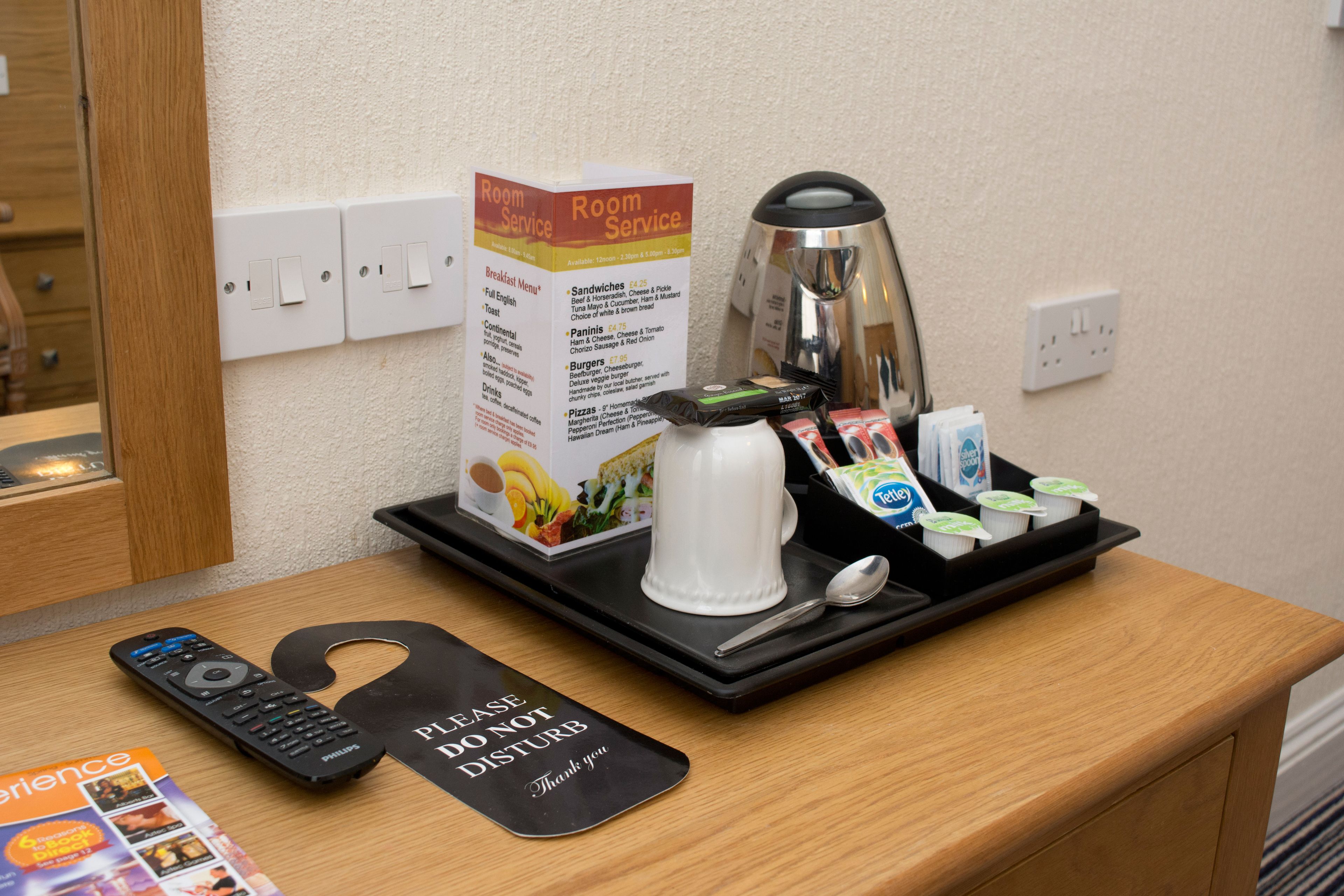 A hotel room with a tray table holding a coffee pot, a remote control, a tray with yogurt cups, and a breakfast menu.