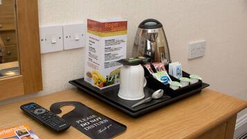 A hotel room with a tray table holding a coffee pot, a remote control, a tray with yogurt cups, and a breakfast menu.