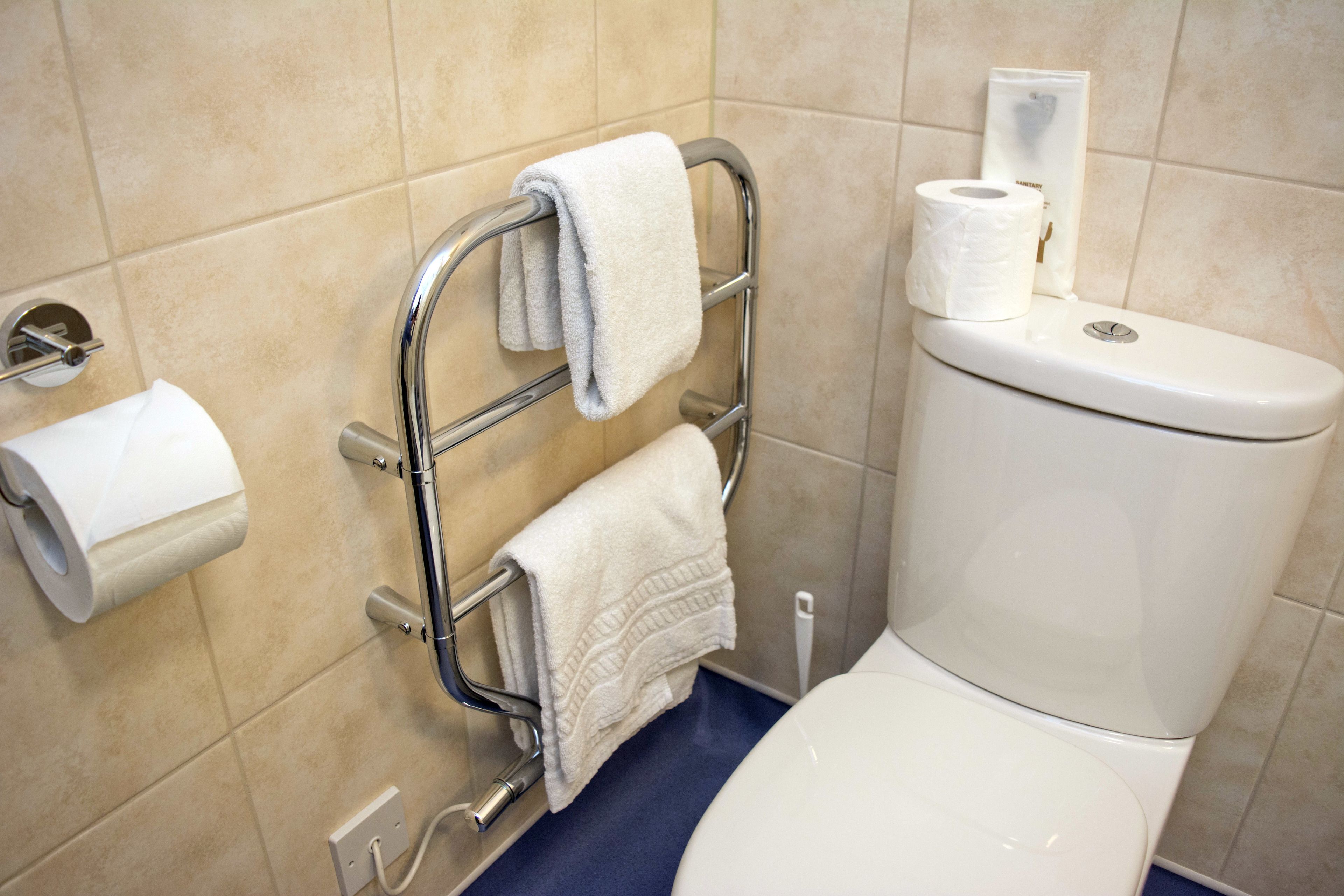 Un baño con inodoro, un perchero con dos toallas y un rollo de papel higiénico en la pared.