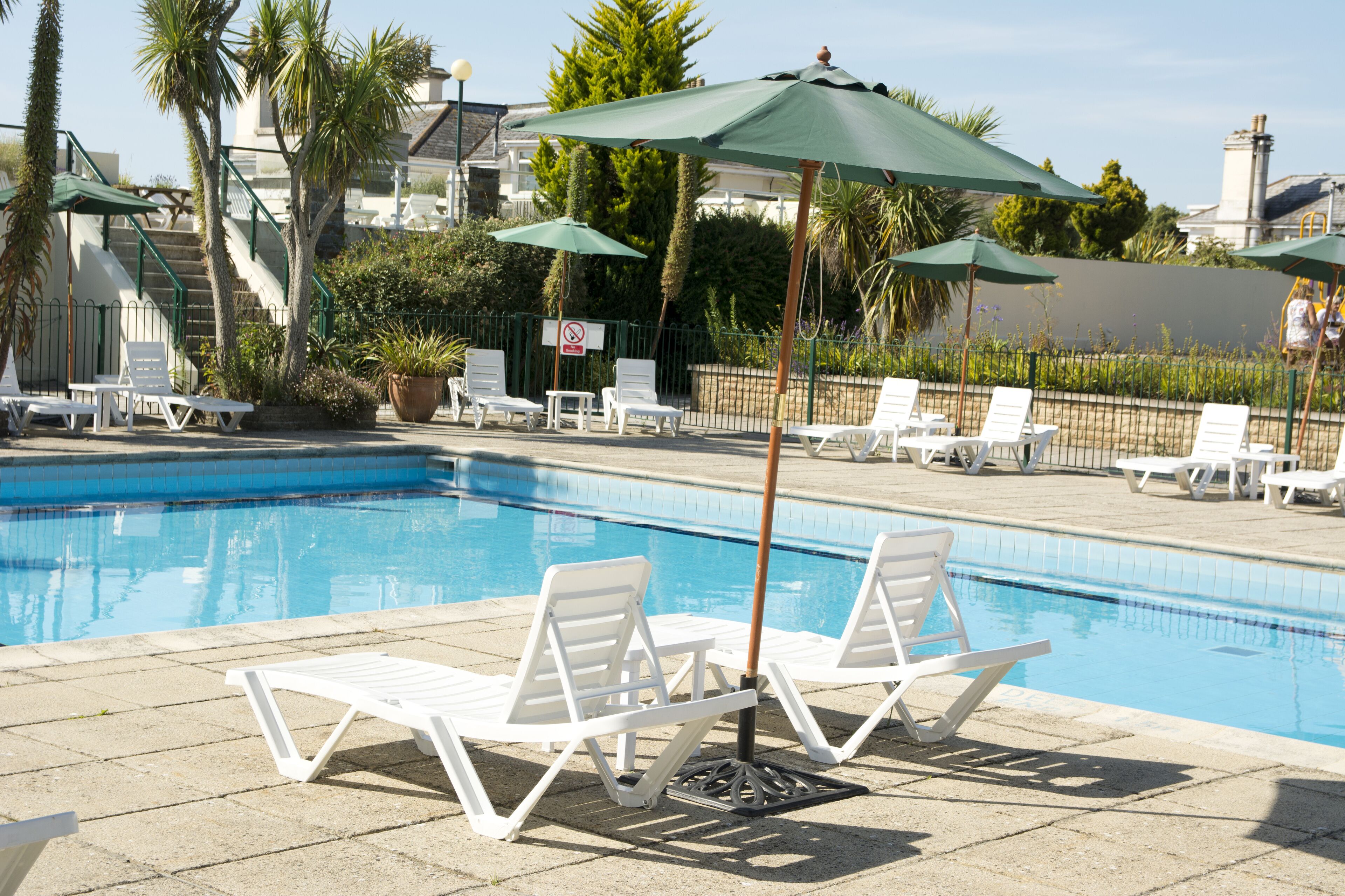 A swimming pool with white lounge chairs and green umbrellas.