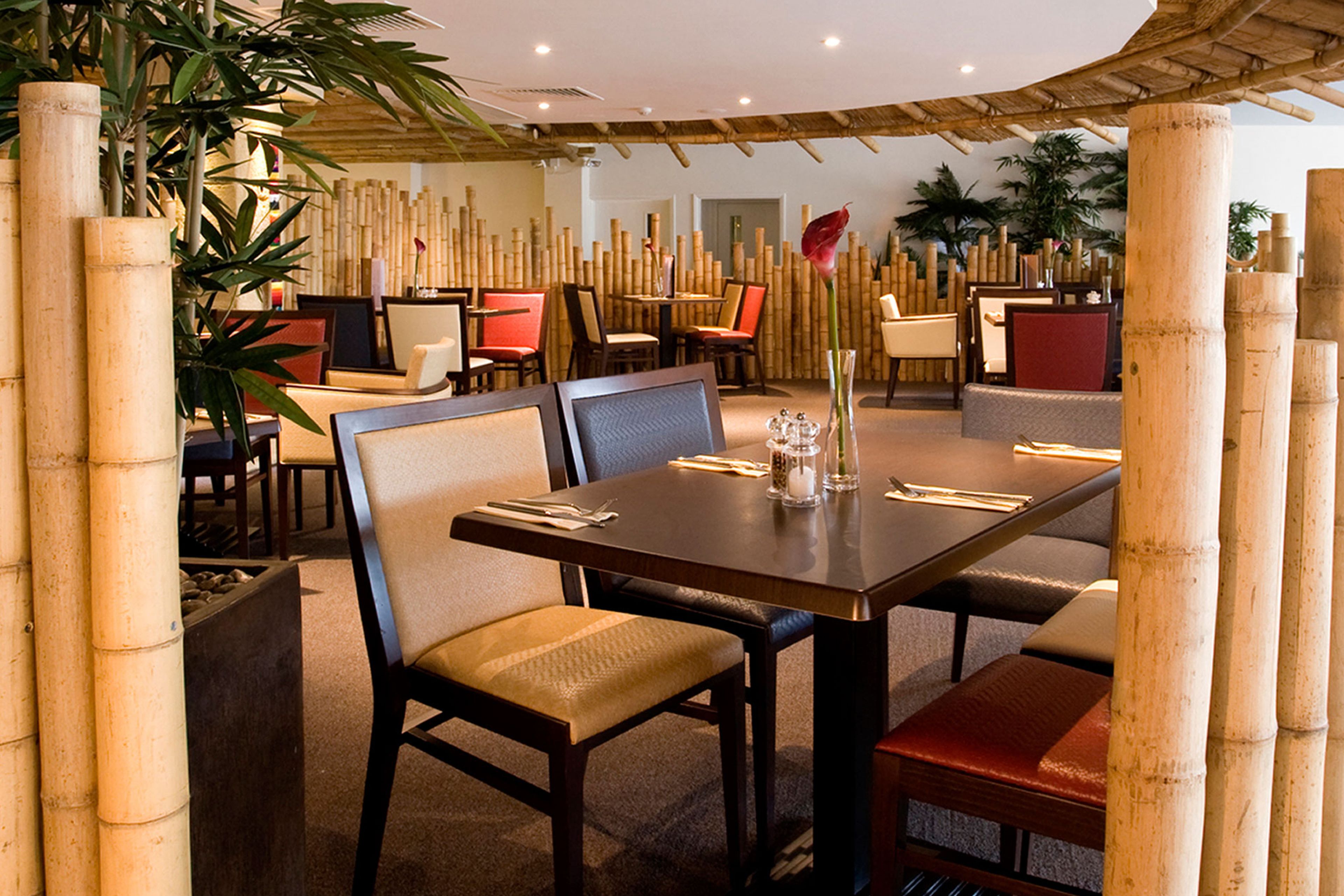 Een restaurant met bamboe-thema, met een grote eettafel en stoelen, omringd door bamboezuilen.