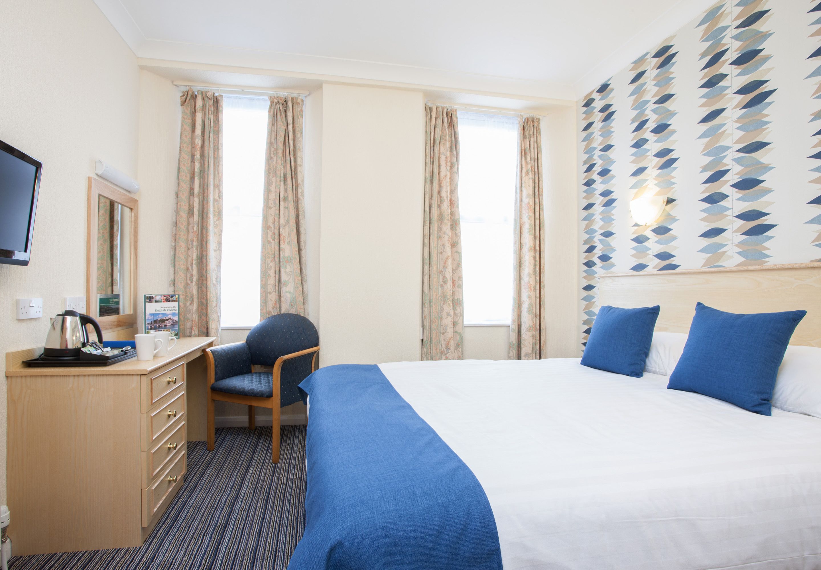 A hotel room with a bed, a desk, a chair, a television, and curtains.