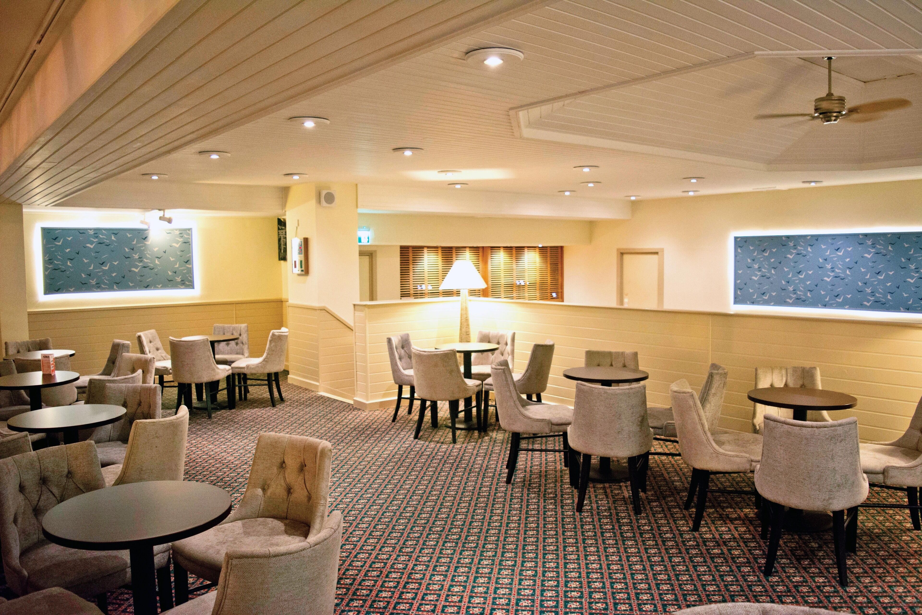 A hotel lobby with multiple seating areas, including round tables and chairs, and a patterned carpet.