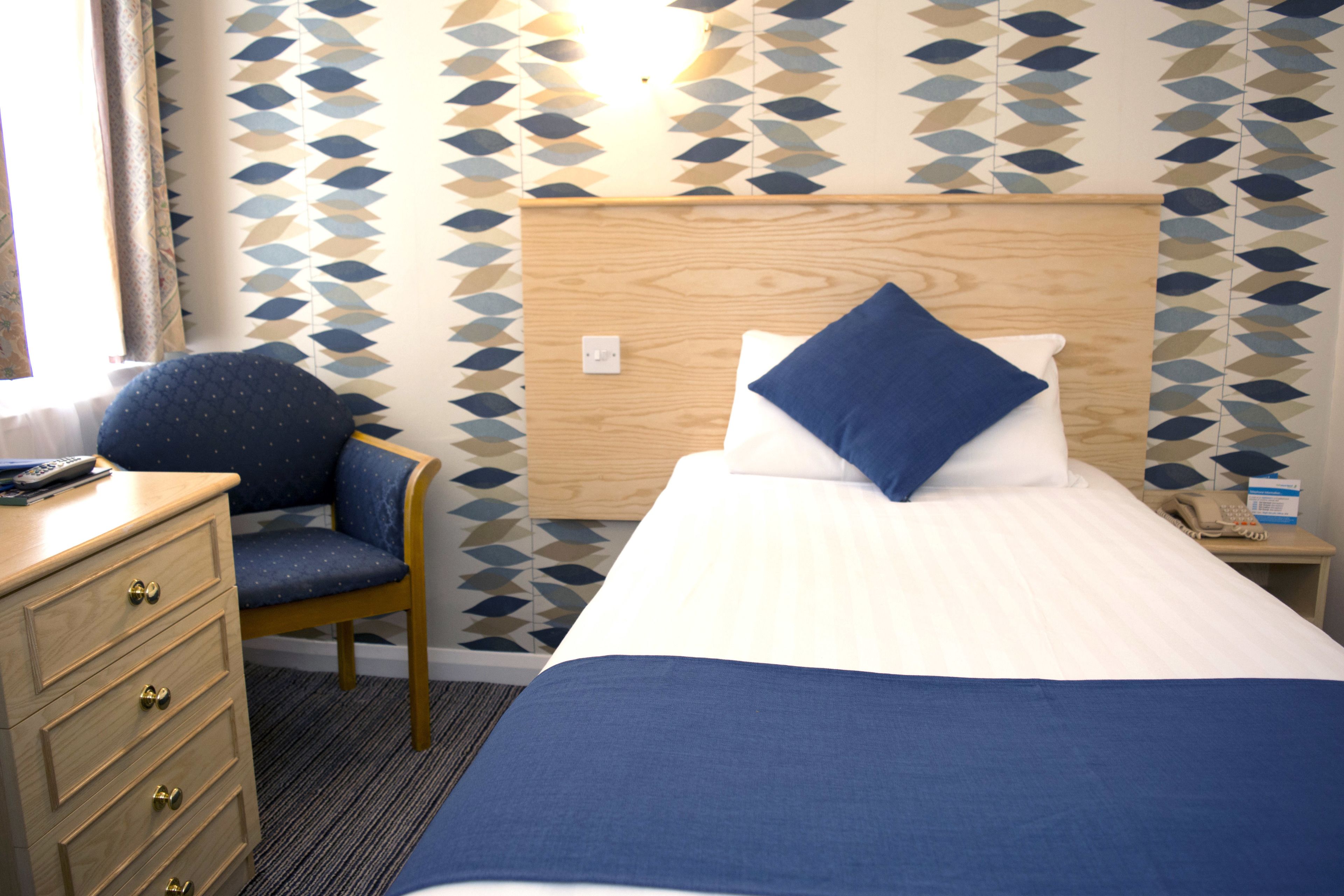 A hotel room with a bed, a chair, a dresser, and a nightstand with a phone.