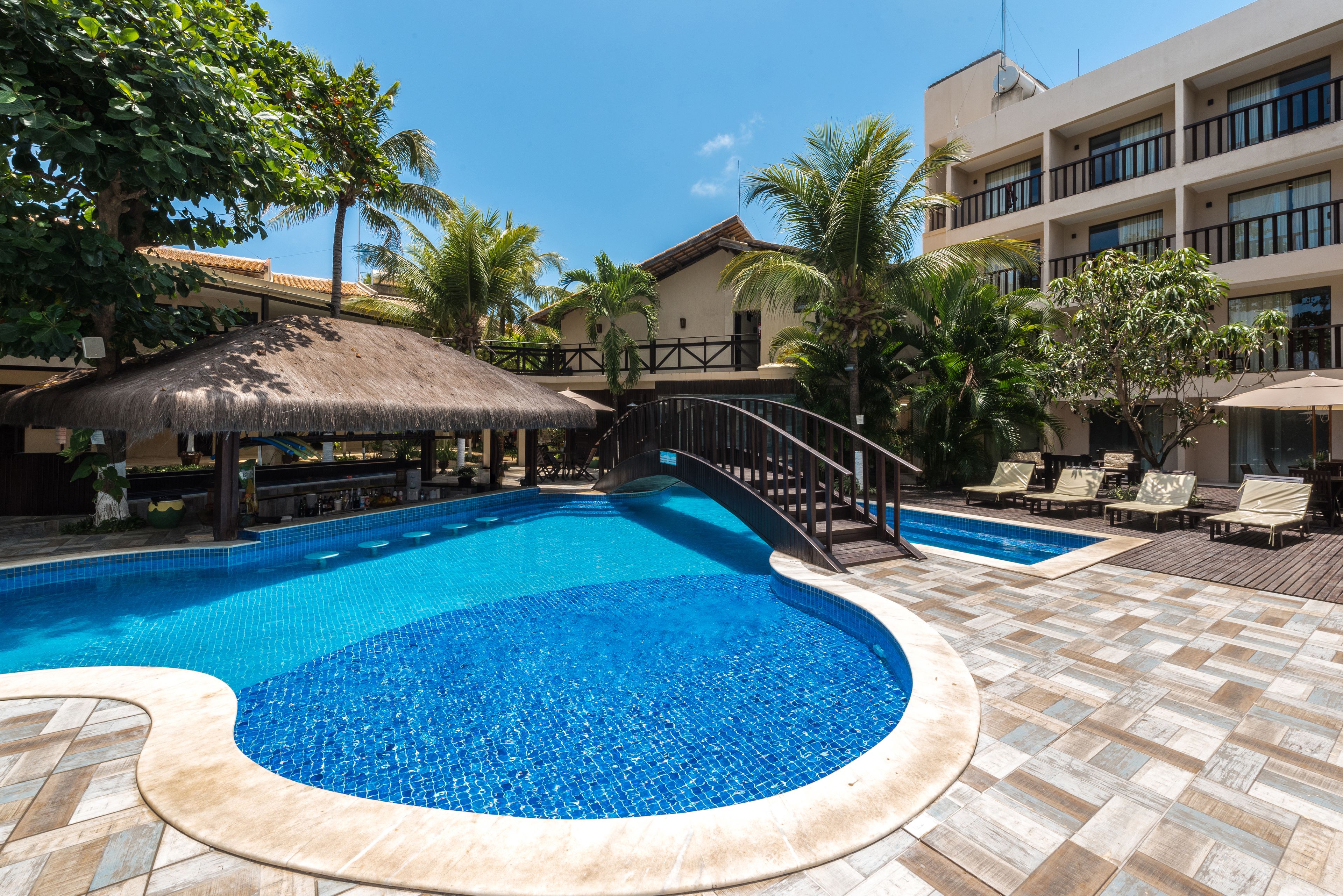 A swimming pool with a thatched roof structure, surrounded by palm trees and lounge chairs.