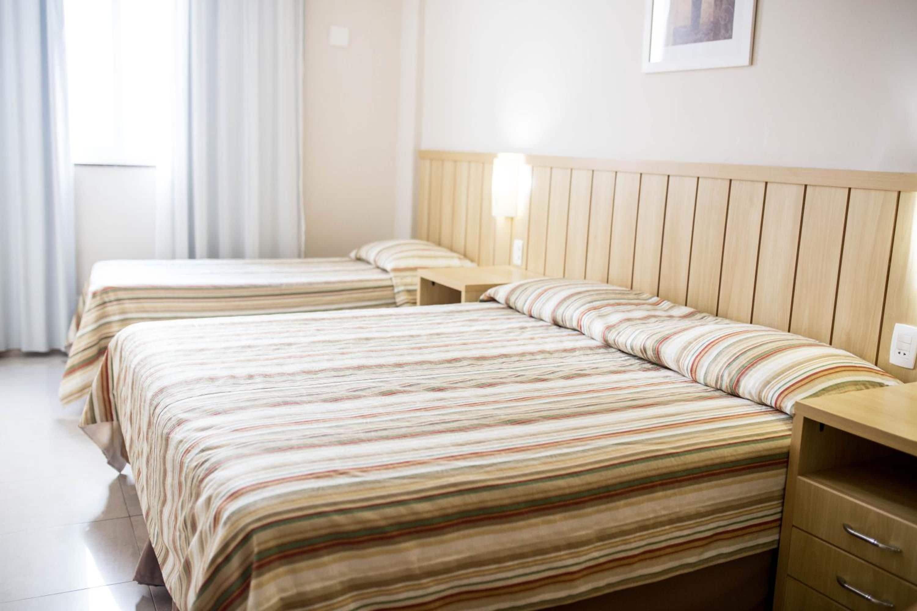 Ein Hotelzimmer mit zwei Betten, einem Holzkopfteil, einem Nachttisch und einer Wandleuchte.