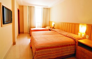 A hotel room with two beds, a TV, a nightstand with a lamp, and a wooden headboard. - Américas Gaivota Hotel (Rio de Janeiro)