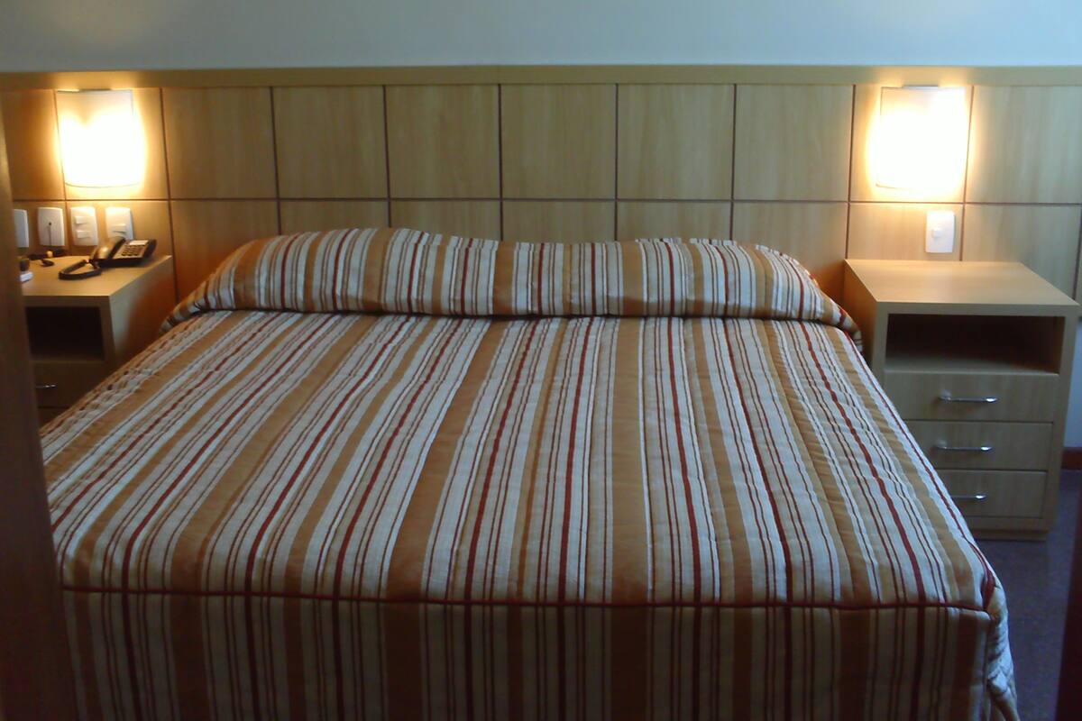 Une chambre d’hôtel avec un grand lit, deux tables de chevet, une petite table avec une lampe et un téléphone fixé au mur.