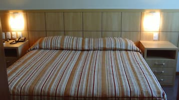 A hotel room with a large bed, two bedside tables, a nightstand with a lamp, and a wall-mounted phone.