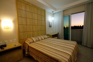 Una camera d'hotel con un letto, una scrivania, una sedia, un telefono e vista sulla città al tramonto.