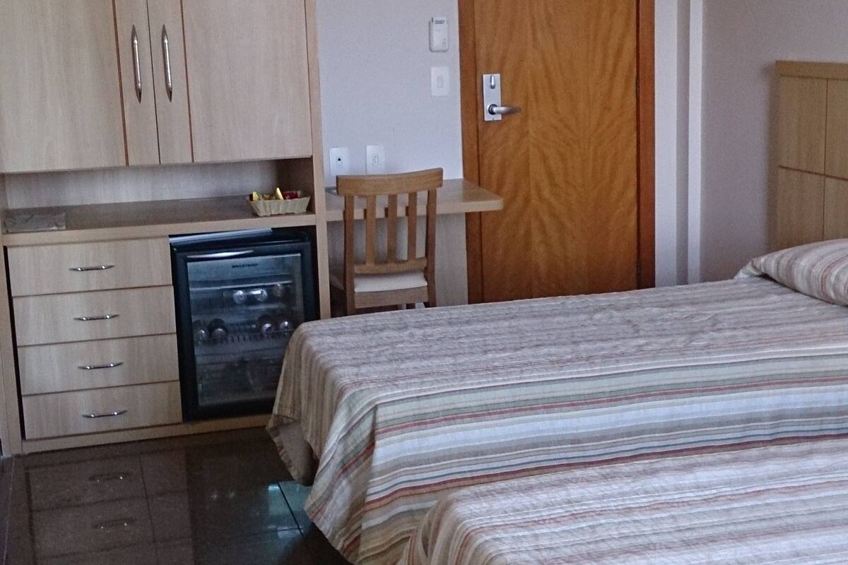 Une chambre avec deux lits, une armoire en bois, une petite table, une chaise et un appareil de climatisation.