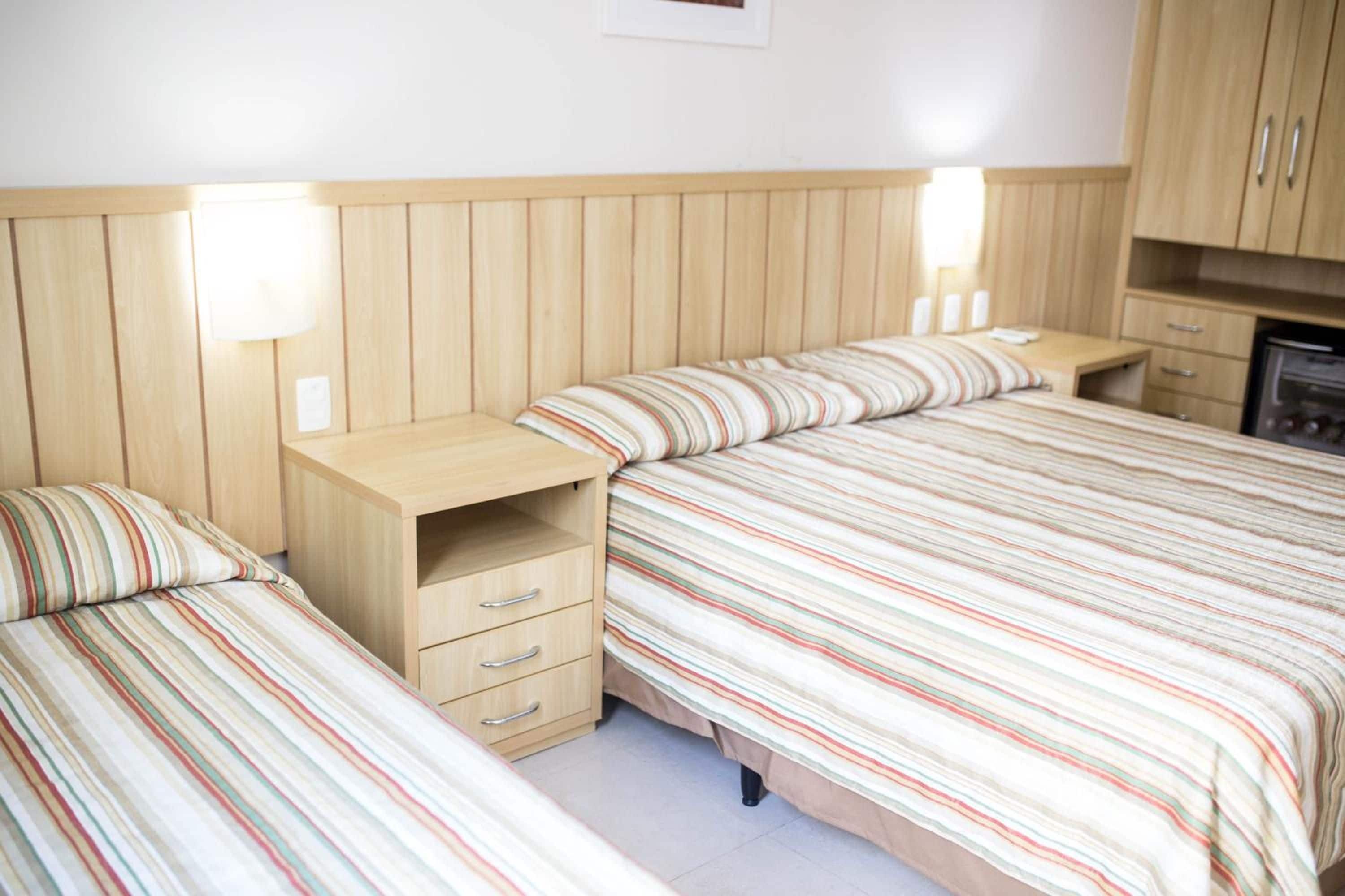 Un dormitorio con dos camas, cabeceros de madera, mesitas de noche y un mueble pequeño.