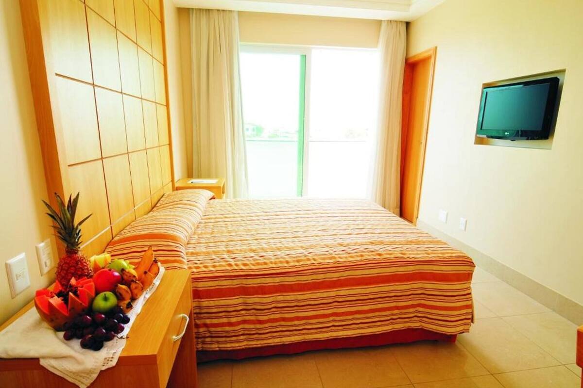 Une chambre d’hôtel avec un lit, un téléviseur fixé au mur et une fenêtre avec des rideaux.