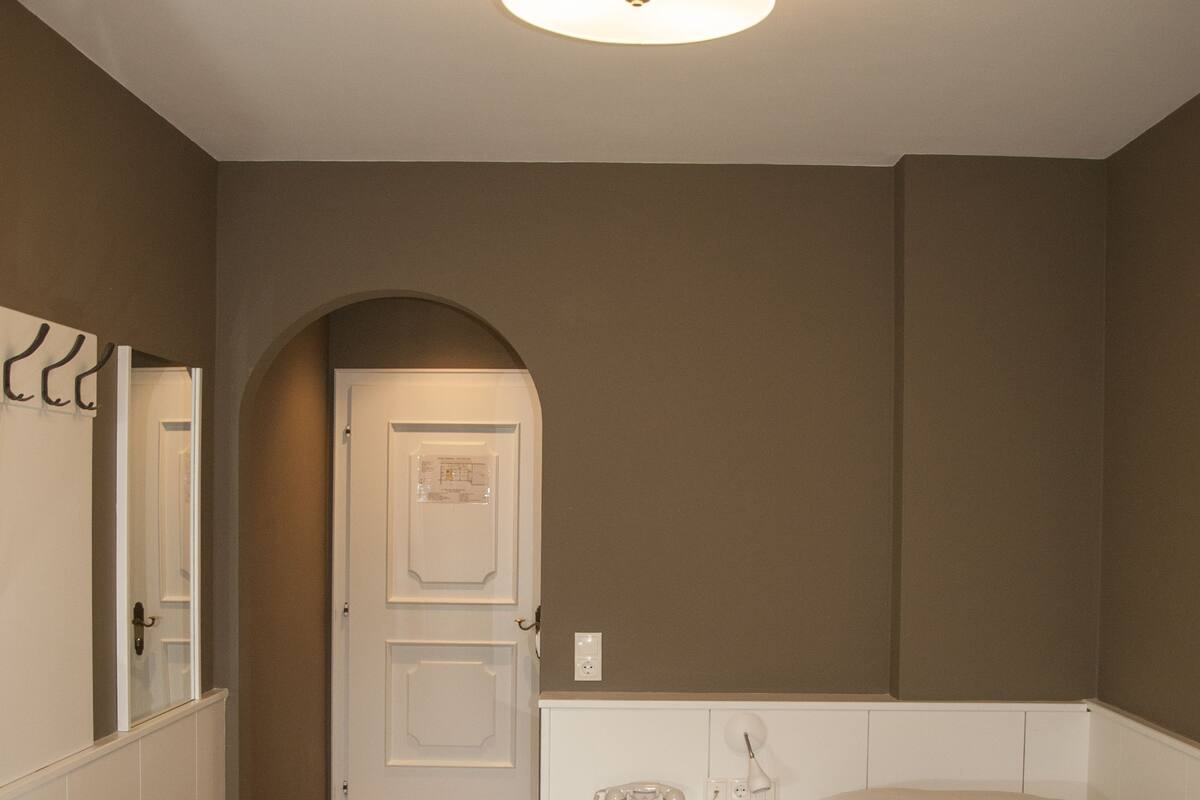 A bedroom with a bed, a desk, a chair, a bedside table, a lamp, and a door.