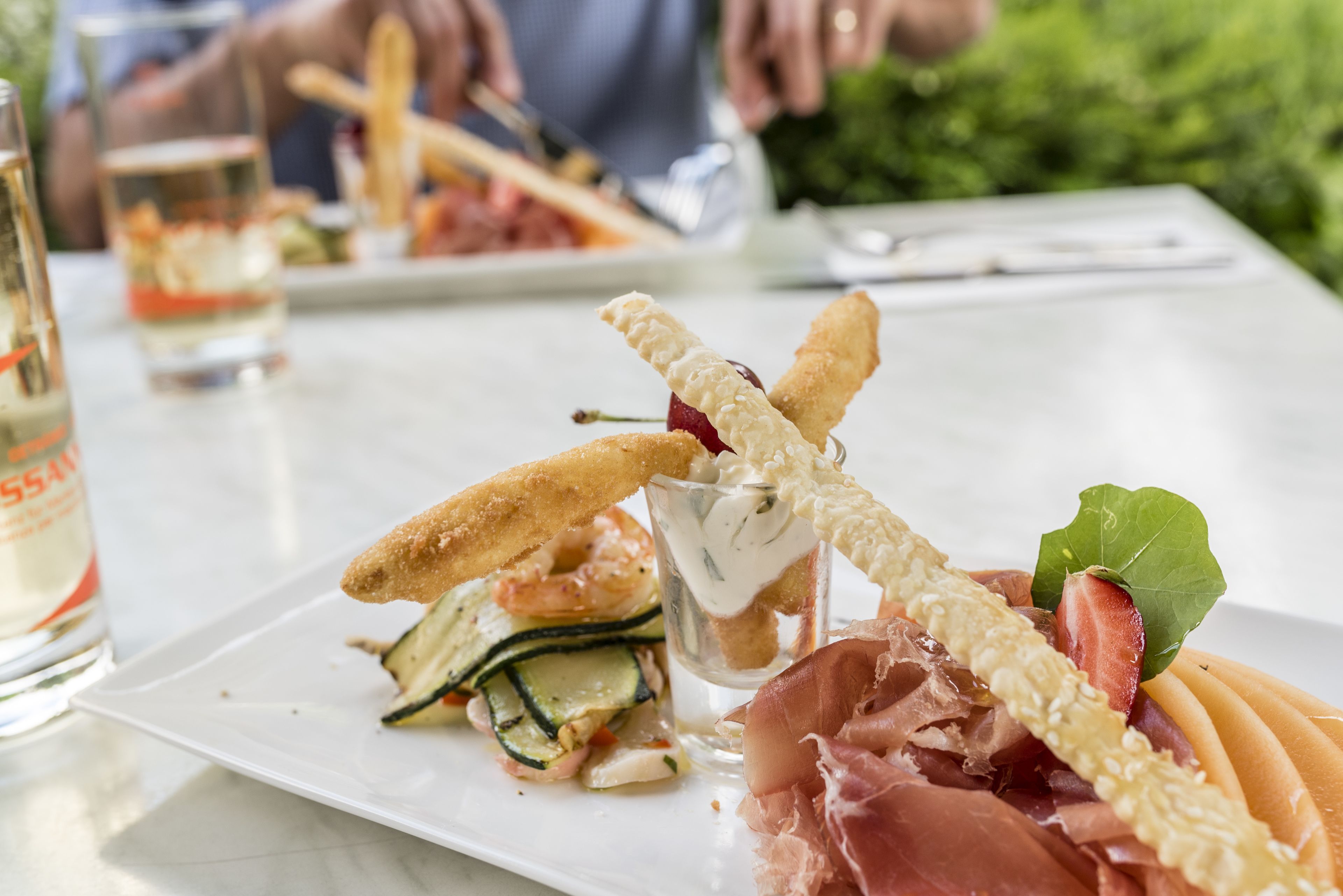 A plate of food with shrimp, vegetables, and prosciutto.