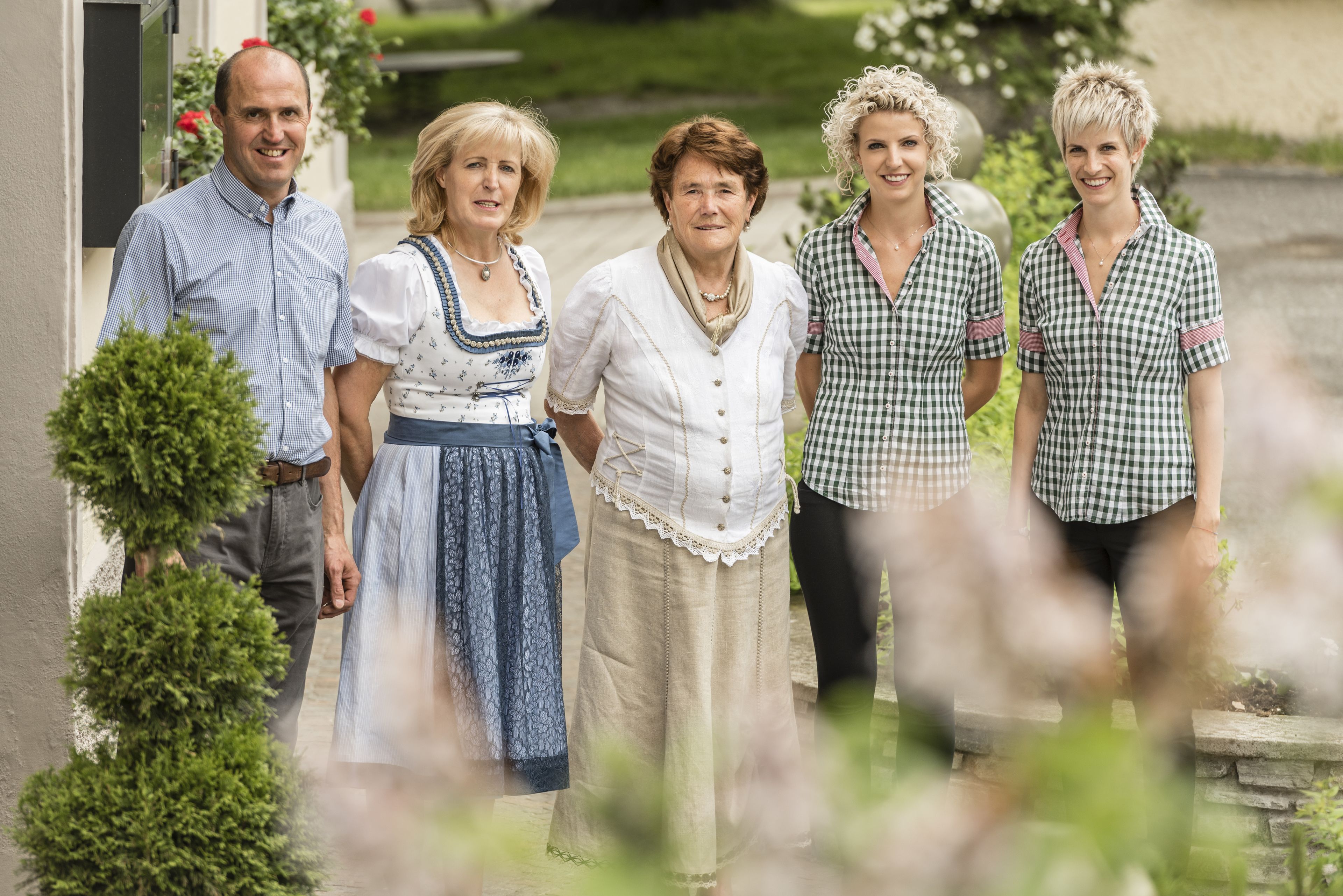 En gruppe mennesker står foran en bygning med en stenvæg og et lille træ.